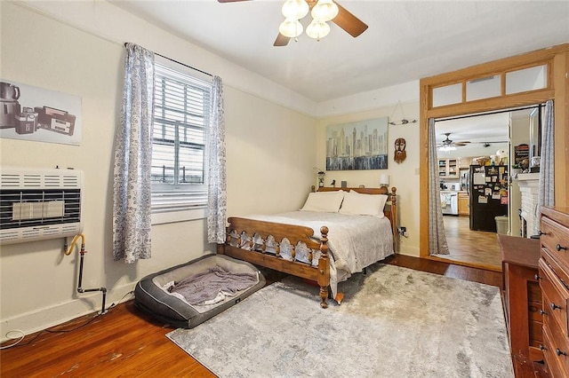 bedroom with heating unit, ceiling fan, dark hardwood / wood-style flooring, and black fridge