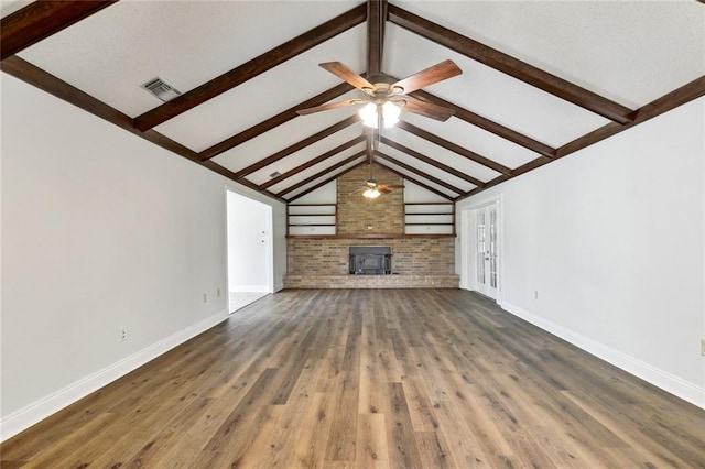 unfurnished living room featuring a wood stove, ceiling fan, brick wall, lofted ceiling with beams, and dark hardwood / wood-style floors