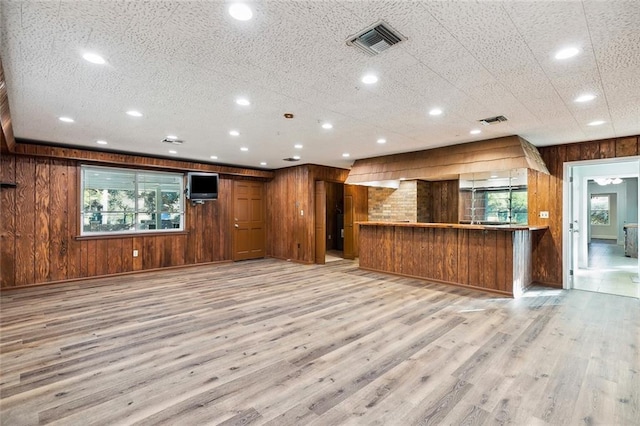 interior space featuring a textured ceiling, light hardwood / wood-style floors, and wooden walls