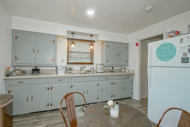 kitchen with pendant lighting, white fridge, sink, and light hardwood / wood-style flooring