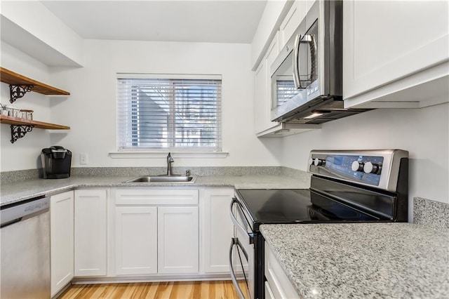 kitchen featuring white cabinets, sink, light hardwood / wood-style flooring, light stone countertops, and appliances with stainless steel finishes