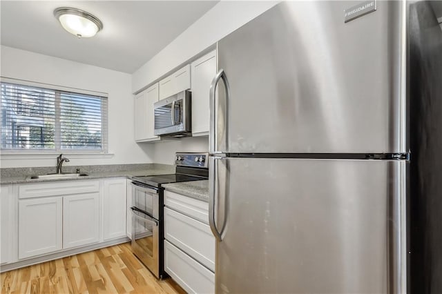 kitchen with sink, white cabinets, light wood-type flooring, and appliances with stainless steel finishes