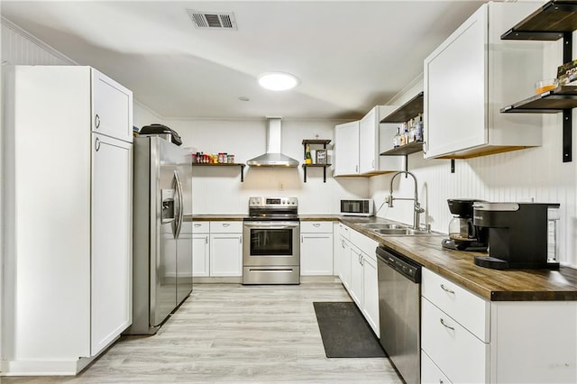 kitchen with wood counters, appliances with stainless steel finishes, wall chimney exhaust hood, light hardwood / wood-style flooring, and white cabinetry