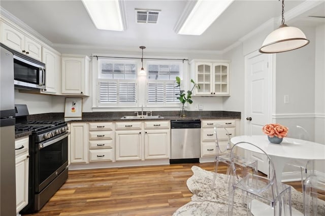 kitchen with sink, light wood-type flooring, decorative light fixtures, appliances with stainless steel finishes, and ornamental molding