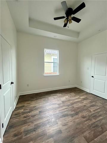 empty room with dark hardwood / wood-style flooring, a tray ceiling, and ceiling fan