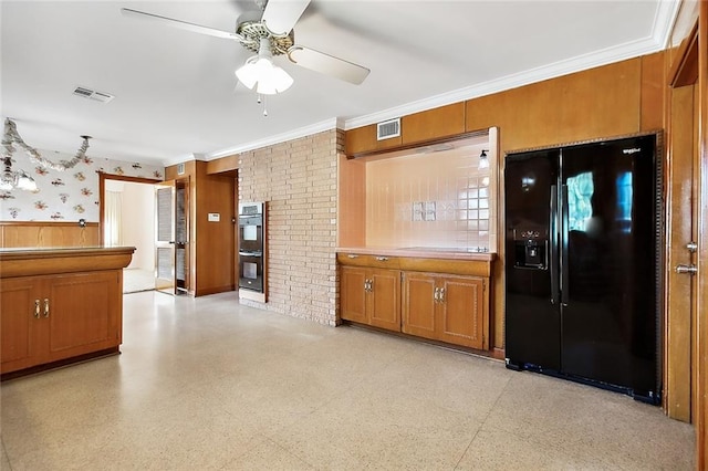 kitchen with wooden walls, ceiling fan, ornamental molding, black fridge with ice dispenser, and stainless steel double oven