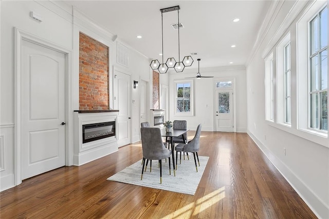 dining area with dark wood-type flooring, a fireplace, a wealth of natural light, and crown molding