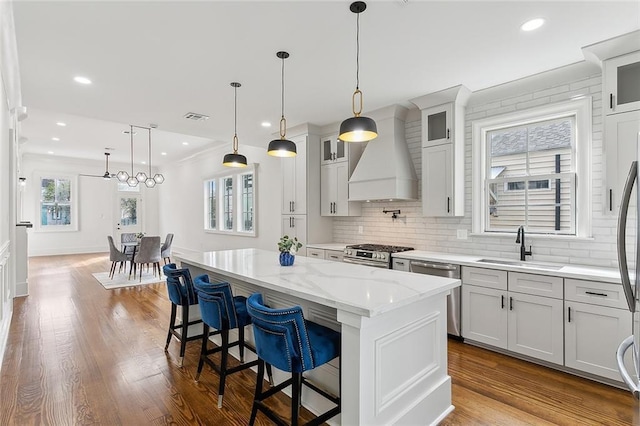 kitchen with pendant lighting, appliances with stainless steel finishes, a kitchen island, sink, and custom range hood