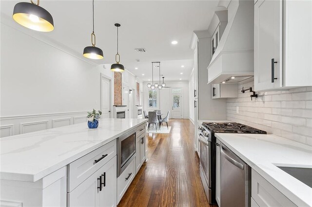 kitchen featuring decorative light fixtures, white cabinets, premium range hood, and stainless steel appliances