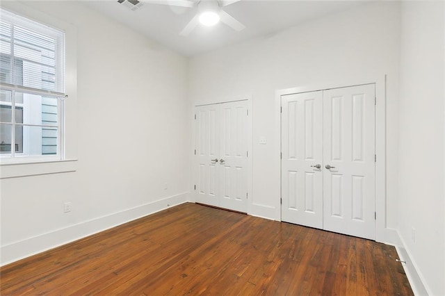 unfurnished bedroom featuring ceiling fan, dark wood-type flooring, and multiple closets