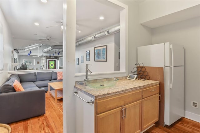 kitchen featuring light stone counters, ceiling fan, sink, light hardwood / wood-style flooring, and white fridge