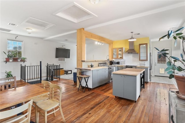 kitchen featuring a center island, wall chimney range hood, tasteful backsplash, wood-type flooring, and gray cabinets