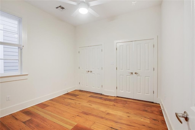 unfurnished bedroom with ceiling fan, light hardwood / wood-style floors, and two closets