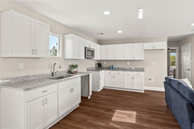 kitchen with light stone countertops, dark hardwood / wood-style flooring, white cabinetry, and sink