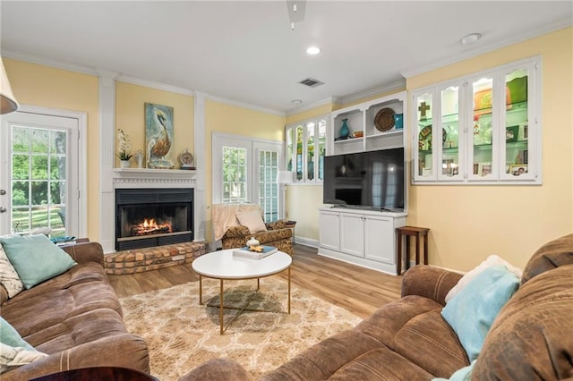 living room with french doors, a brick fireplace, light hardwood / wood-style flooring, ceiling fan, and ornamental molding