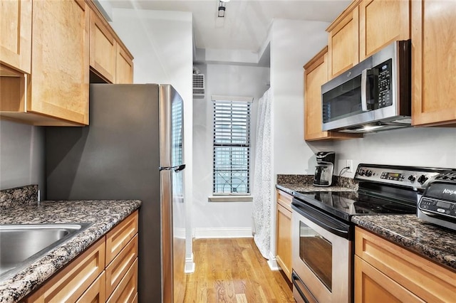 kitchen with stainless steel appliances, light hardwood / wood-style flooring, and dark stone counters