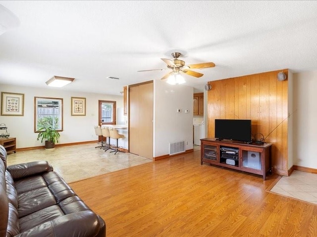 living room featuring wood walls, ceiling fan, a textured ceiling, and light wood-type flooring