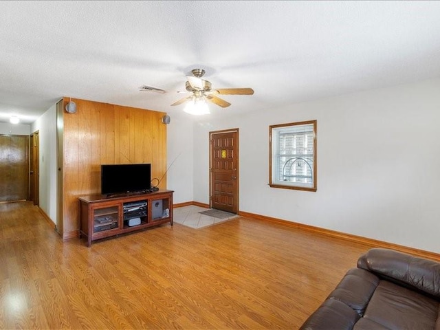 living room with wooden walls, ceiling fan, light hardwood / wood-style floors, and a textured ceiling