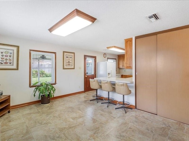 kitchen featuring a textured ceiling, a kitchen bar, white refrigerator with ice dispenser, and kitchen peninsula