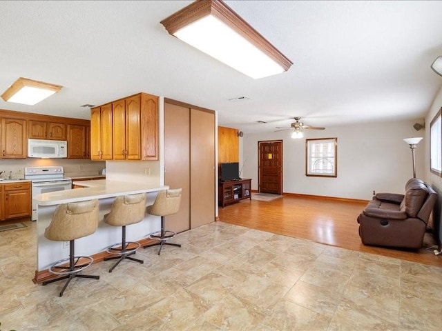 kitchen featuring kitchen peninsula, a kitchen breakfast bar, white appliances, ceiling fan, and light hardwood / wood-style flooring