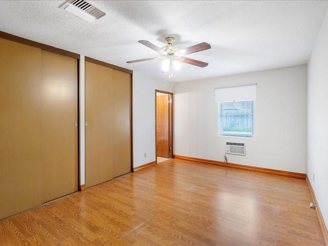 unfurnished bedroom featuring ceiling fan, light hardwood / wood-style flooring, an AC wall unit, a textured ceiling, and two closets