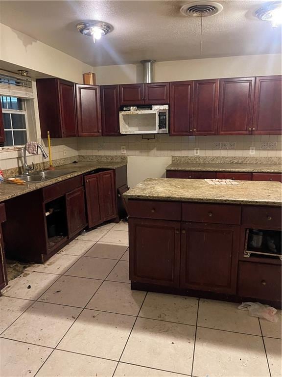 kitchen featuring sink, a textured ceiling, tasteful backsplash, light tile patterned flooring, and light stone counters