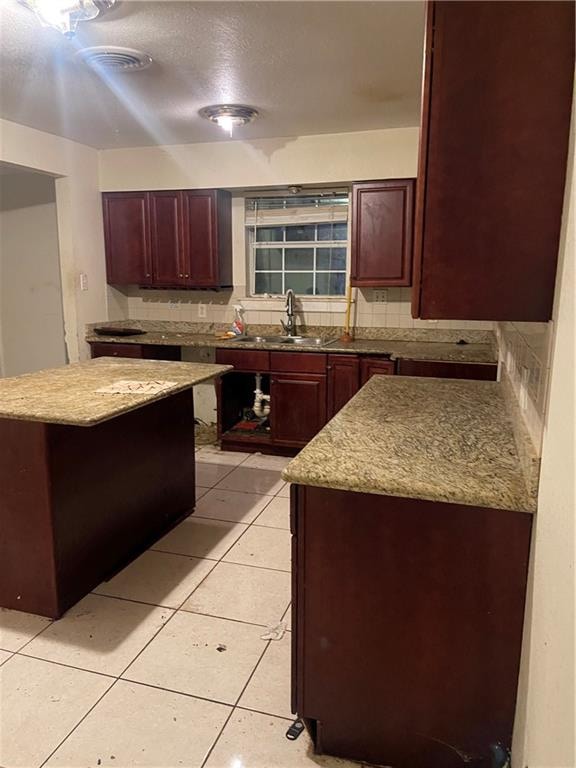 kitchen featuring decorative backsplash, light tile patterned flooring, a kitchen island, and sink