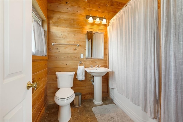 bathroom featuring wooden walls, tile patterned flooring, shower / tub combo, and toilet