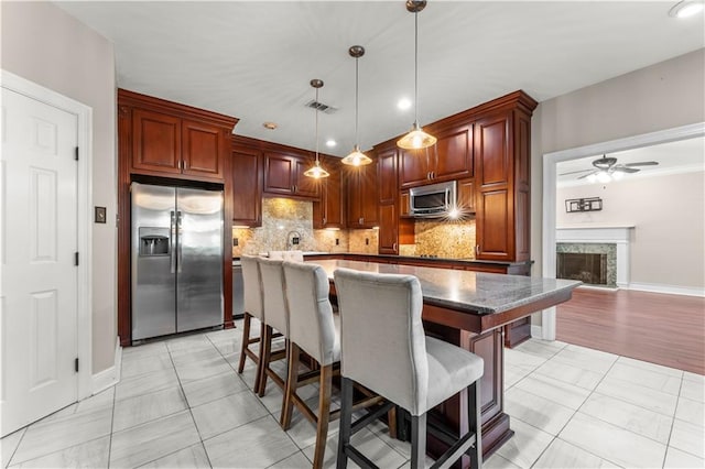 kitchen with stainless steel appliances, ceiling fan, pendant lighting, a premium fireplace, and a center island