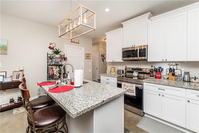 kitchen with light stone counters, white cabinetry, stainless steel appliances, and an island with sink