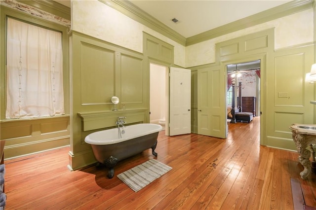 bathroom with hardwood / wood-style floors, a tub to relax in, toilet, and crown molding