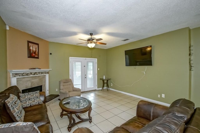 living room with a tile fireplace, ceiling fan, light tile patterned floors, and a textured ceiling