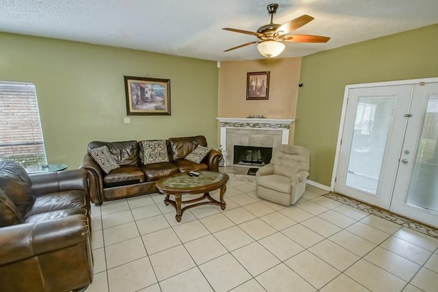 living room with a tile fireplace, ceiling fan, french doors, and light tile patterned flooring