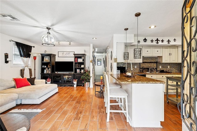 kitchen featuring a kitchen bar, dark stone countertops, light wood-type flooring, and hanging light fixtures