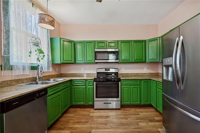 kitchen featuring sink, stainless steel appliances, light stone counters, pendant lighting, and light wood-type flooring