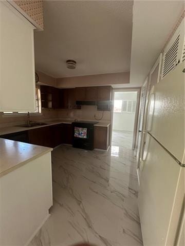 kitchen featuring dark brown cabinetry, sink, range hood, white fridge, and black range