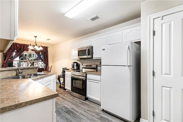 kitchen with white cabinetry, sink, a notable chandelier, hardwood / wood-style floors, and appliances with stainless steel finishes