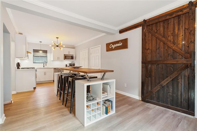 kitchen featuring white cabinetry, stainless steel microwave, a barn door, pendant lighting, and light hardwood / wood-style floors