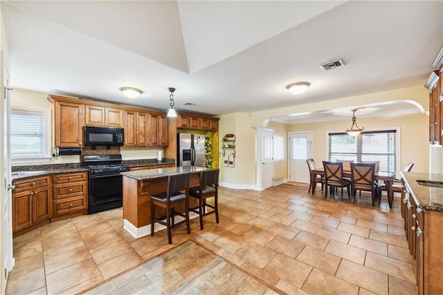 kitchen featuring a center island, dark stone counters, black appliances, hanging light fixtures, and a breakfast bar area