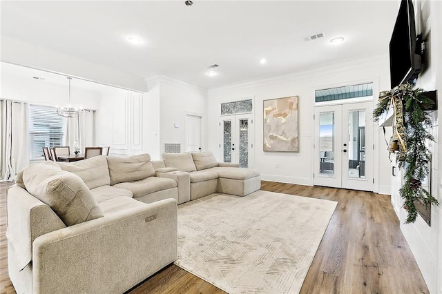 living room featuring hardwood / wood-style flooring, a notable chandelier, crown molding, and french doors