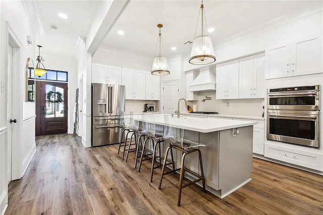 kitchen featuring a kitchen breakfast bar, stainless steel appliances, a kitchen island with sink, white cabinets, and hardwood / wood-style floors