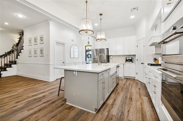 kitchen with hardwood / wood-style flooring, white cabinets, an island with sink, and stainless steel appliances