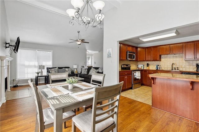 dining space with sink, crown molding, high vaulted ceiling, light wood-type flooring, and ceiling fan with notable chandelier