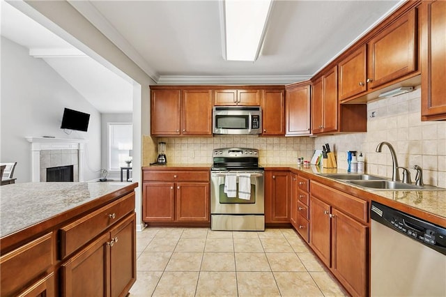 kitchen with sink, light tile patterned floors, stainless steel appliances, a tiled fireplace, and decorative backsplash