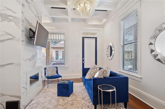 living room with beamed ceiling, dark hardwood / wood-style flooring, an inviting chandelier, and coffered ceiling