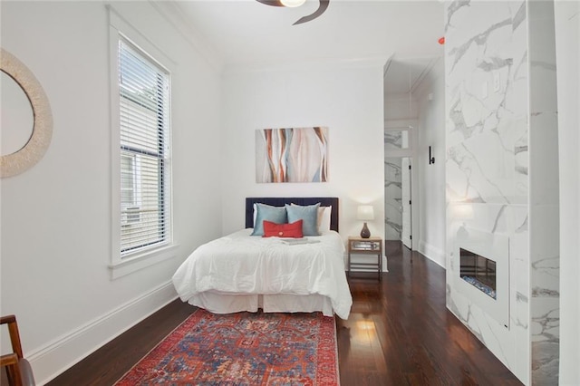 bedroom with crown molding, a fireplace, ceiling fan, and dark wood-type flooring