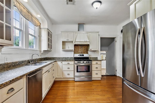 kitchen featuring sink, stainless steel appliances, dark stone counters, light hardwood / wood-style floors, and white cabinets