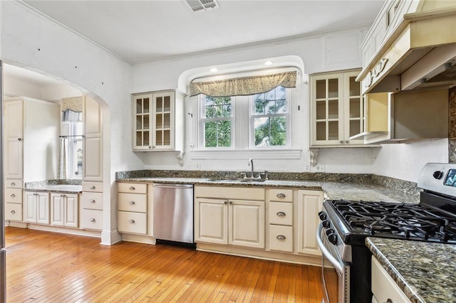 kitchen featuring stainless steel appliances, premium range hood, light hardwood / wood-style floors, cream cabinetry, and ornamental molding