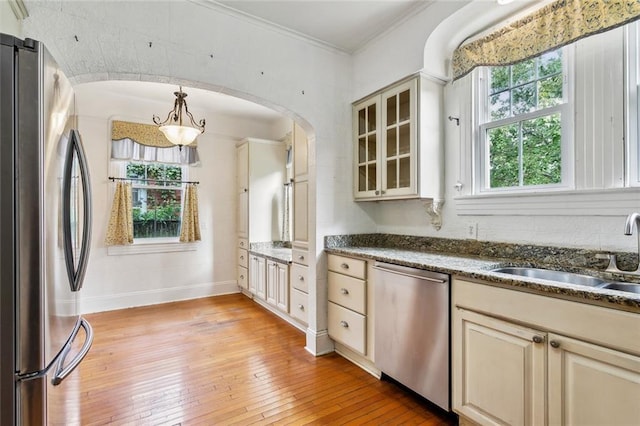 kitchen with appliances with stainless steel finishes, sink, cream cabinets, light hardwood / wood-style floors, and hanging light fixtures