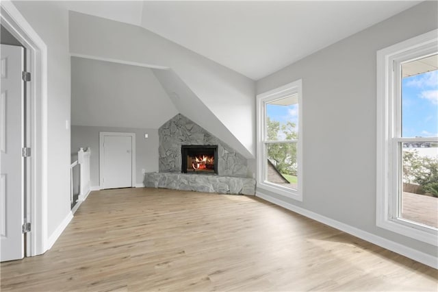 additional living space featuring a fireplace, lofted ceiling, light wood-type flooring, and a healthy amount of sunlight